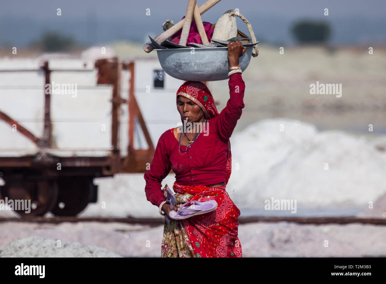 SAMBHAR, INDIEN - November 19, 2012: Indische Frau mittleren Alters trägt ein Becken mit Instrumenten auf den Kopf. Frau raucht, während die Becken auf den Kopf Stockfoto