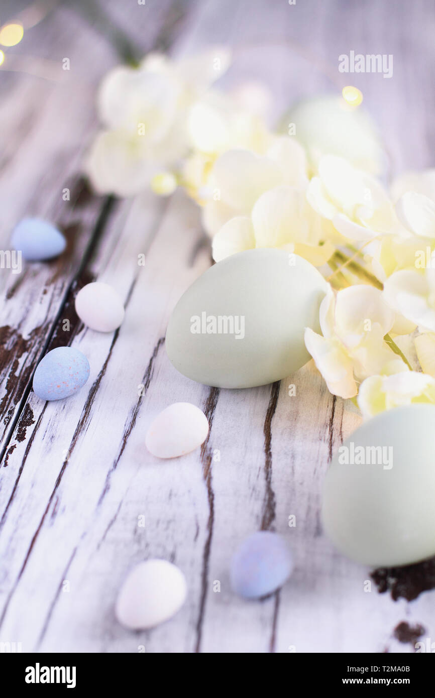 Natürlich gefärbten Ostereier, Malz Bonbon, Schokolade, Eier, und Blüten über eine rustikale weißem Holz Tisch/Hintergrund. Stockfoto