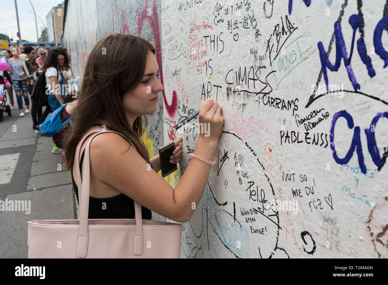 Berlin. Deutschland. Eine junge Frau, die ihre Markierung an der Berliner Mauer an der East Side Gallery. Stockfoto