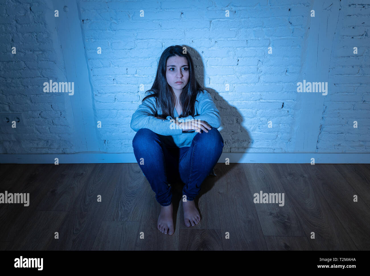 Porträt der jungen verzweifelten Latin Frau Gefühl miserabel, einsam, hoffnungslos und traurig, auf dem Boden sitzend gegen eine weiße Wand mit Kopie Raum und moo Stockfoto