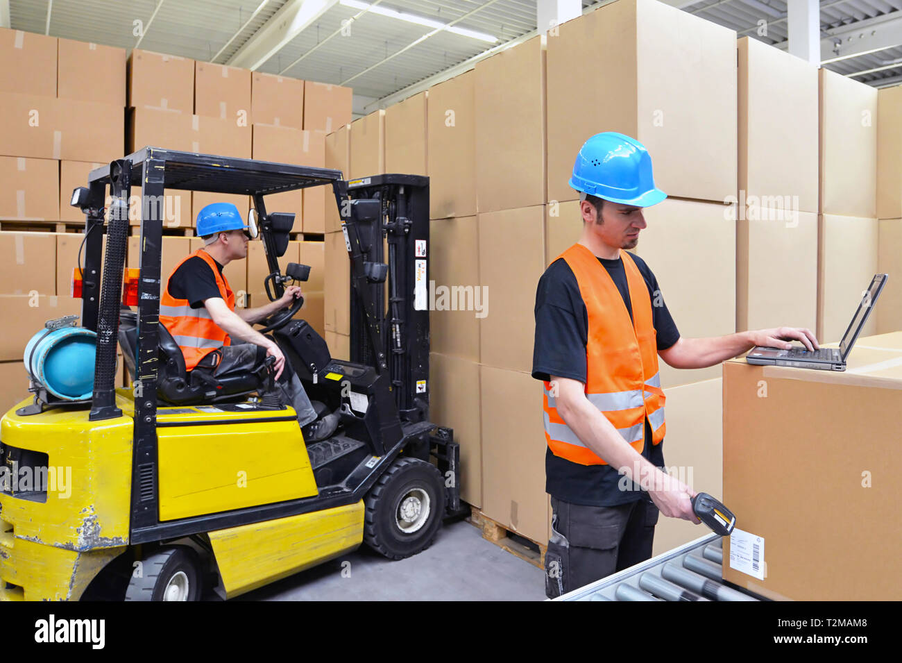 Arbeiter mit Notebook und Barcode Scanner verarbeitet eine Sendung im Kaufhaus - Gabelstaplerfahrer im Hintergrund Stockfoto