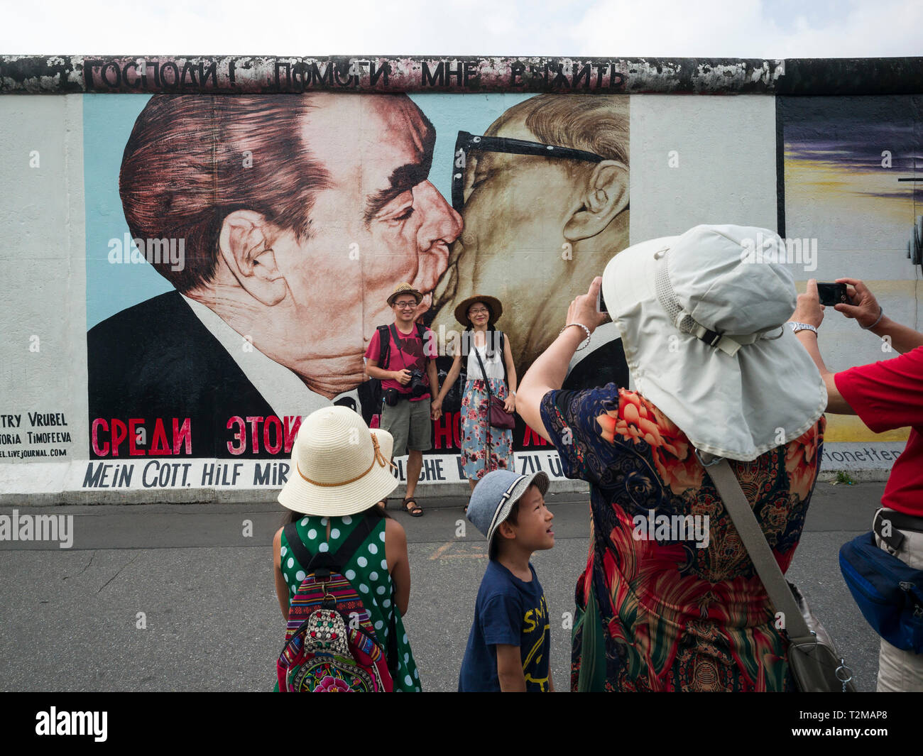 Berlin. Deutschland. Touristen posieren für Fotos vor einem der übrigen Abschnitte der Berliner Mauer an der East Side Gallery. Touristen posieren für ph Stockfoto