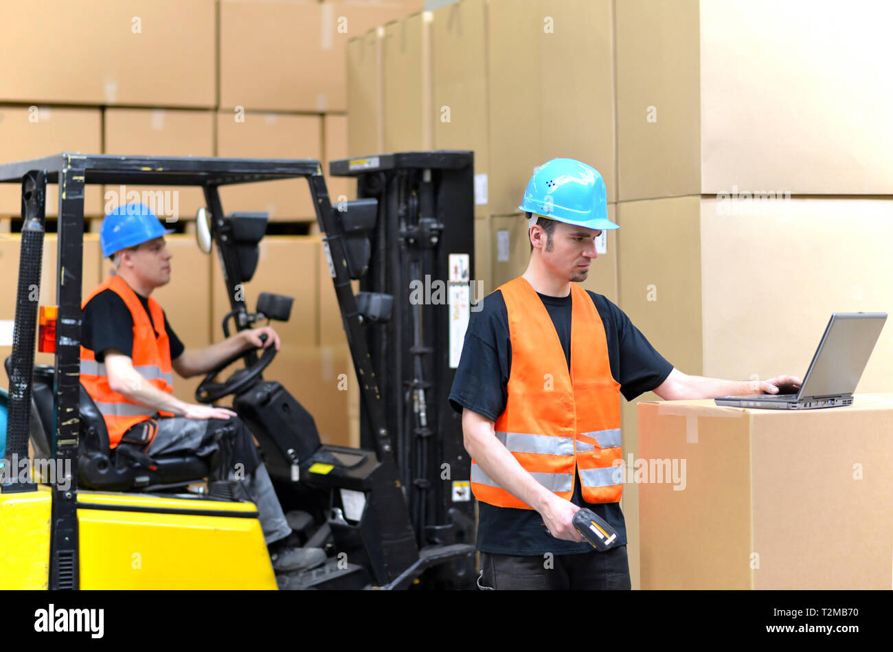 Arbeiter mit Notebook und Barcode Scanner verarbeitet eine Sendung im Kaufhaus - Gabelstaplerfahrer im Hintergrund Stockfoto