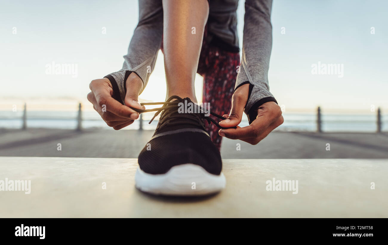 Frau band ihre Schnürsenkel vor einem Lauf. Läuferin ihre Schnürsenkel binden beim Training im Freien auf einer Straße durch das Meer. Stockfoto