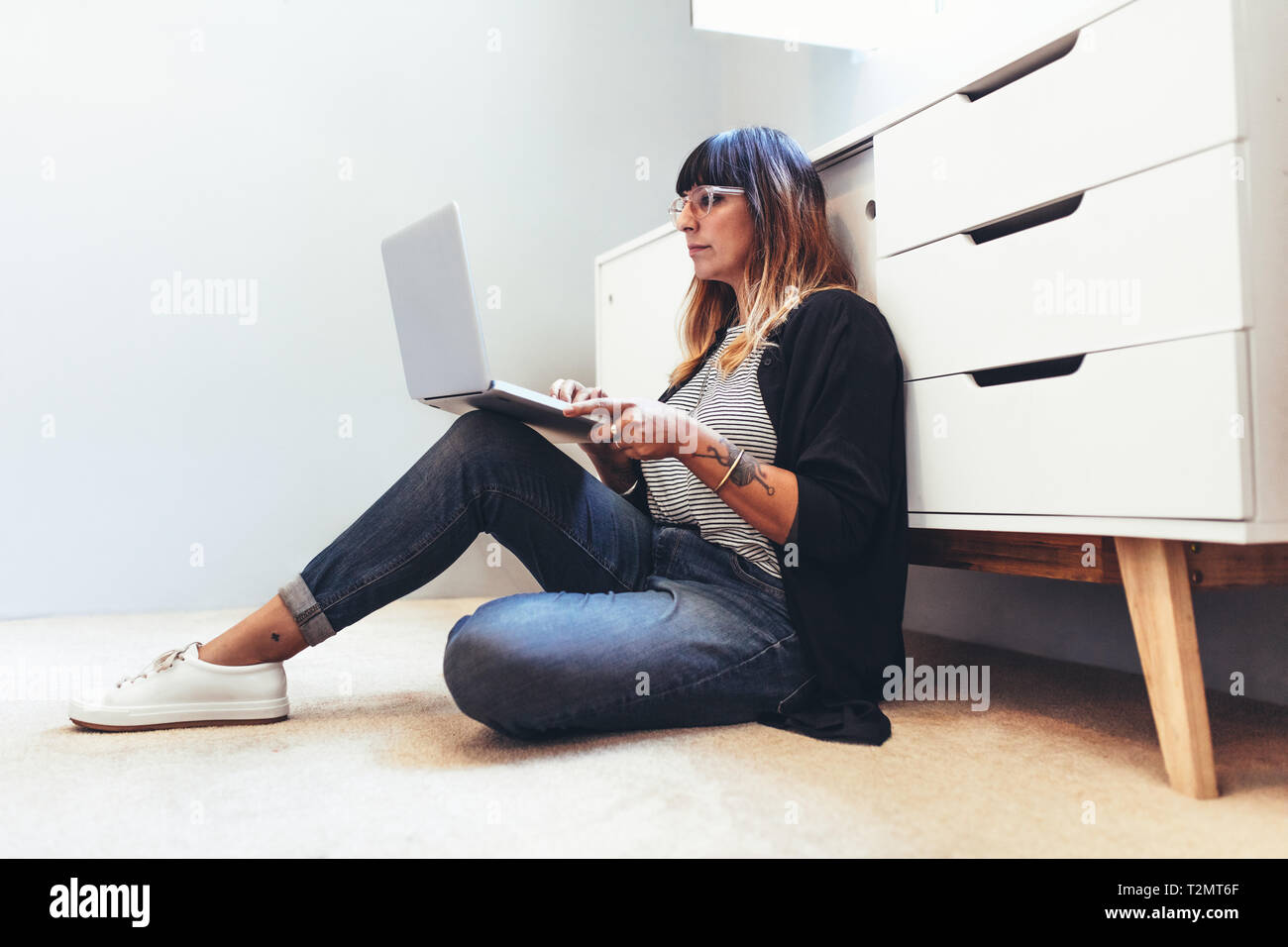 Freie Frau, die Arbeiten am Laptop sitzen auf dem Boden. Weibliche Unternehmer sitzen auf dem Boden arbeiten von zu Hause aus. Stockfoto
