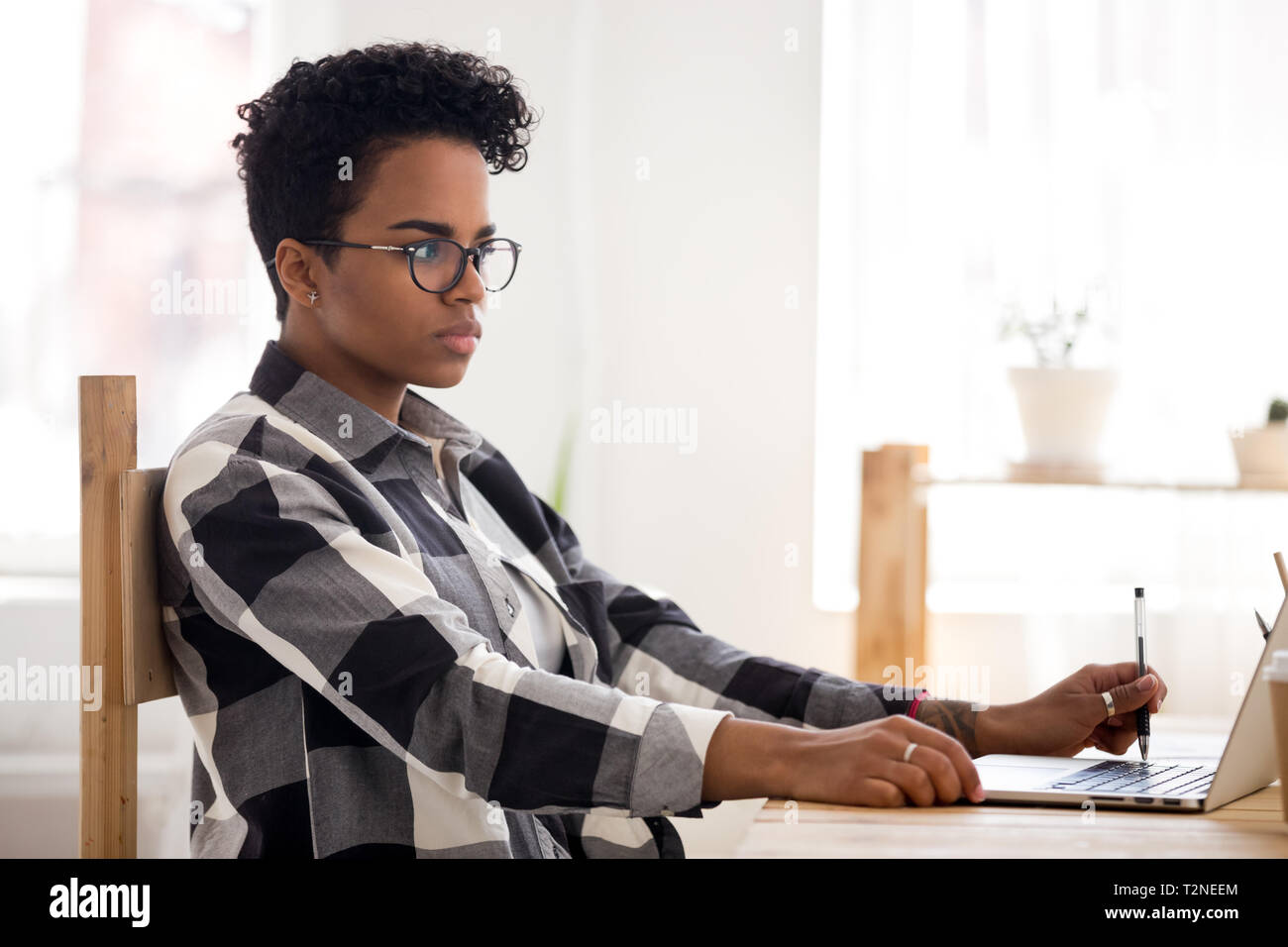 Konzentriert afrikanischen tausendjährigen Frau mit Brille am Schreibtisch im Büro sitzen nur Arbeiten mit Laptop. Junge ernster Kursteilnehmer oder Business Stockfoto
