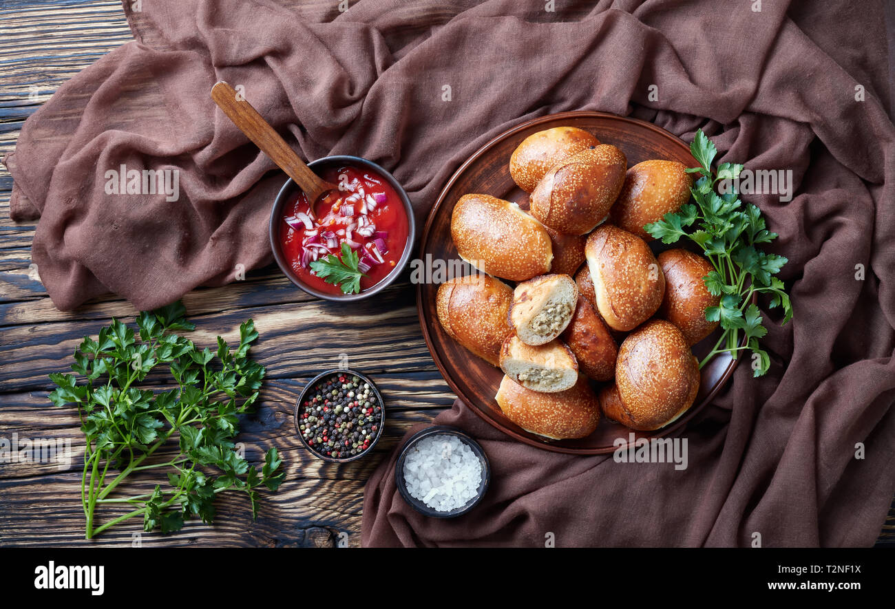 Frisch gebackenes Brot Teig Umsätze mit Schweine- und Hühnerfleisch füllen, portablen Pocket Sandwiches auf einem Schild an einem Holztisch mit braunen Klumpen Stockfoto