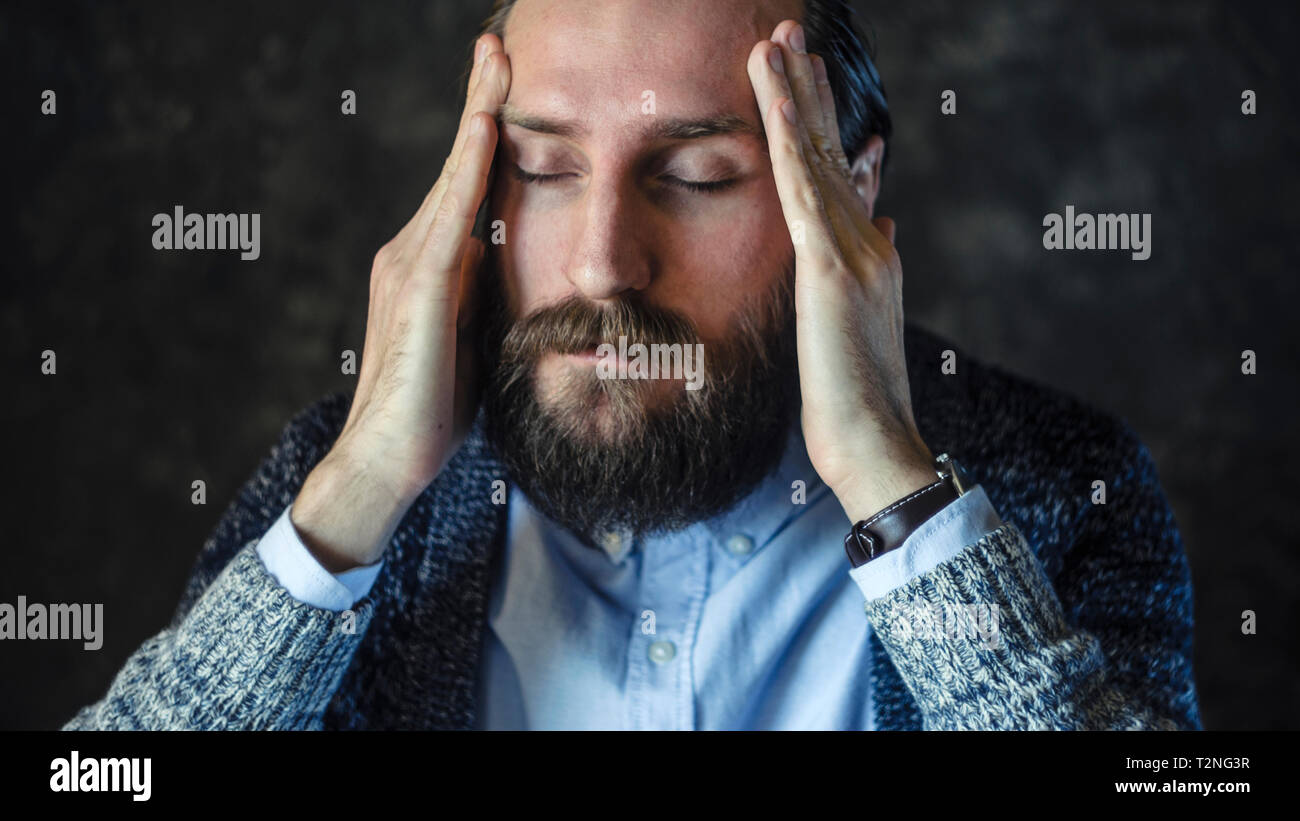 Portrait von nachdenklich, bärtiger Mann im blauen T-Shirt und Strickjacke mit geschlossenen Augen, hielt seinen Tempel. Versuchen Sie, das Konzept zu erinnern Stockfoto
