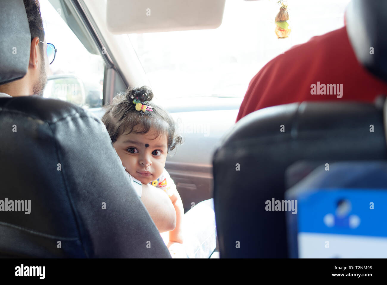 Einen schönen Indischen Baby Mädchen Kind im Auto vorne sitzen ist Blick auf etwas auf dem Rücksitz in einem fahrenden Auto. Indische Lebensstil Stockfoto