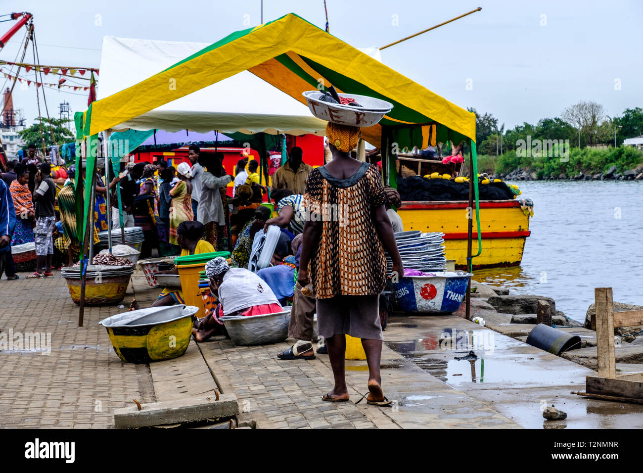 SEKONDI TAKORADI, GHANA - 10. APRIL 2018: Pulsierende Hafen angeln Markt Szene als Frau in Buntes Kleid trägt Korb auf dem Kopf bereit zu pr sammeln Stockfoto