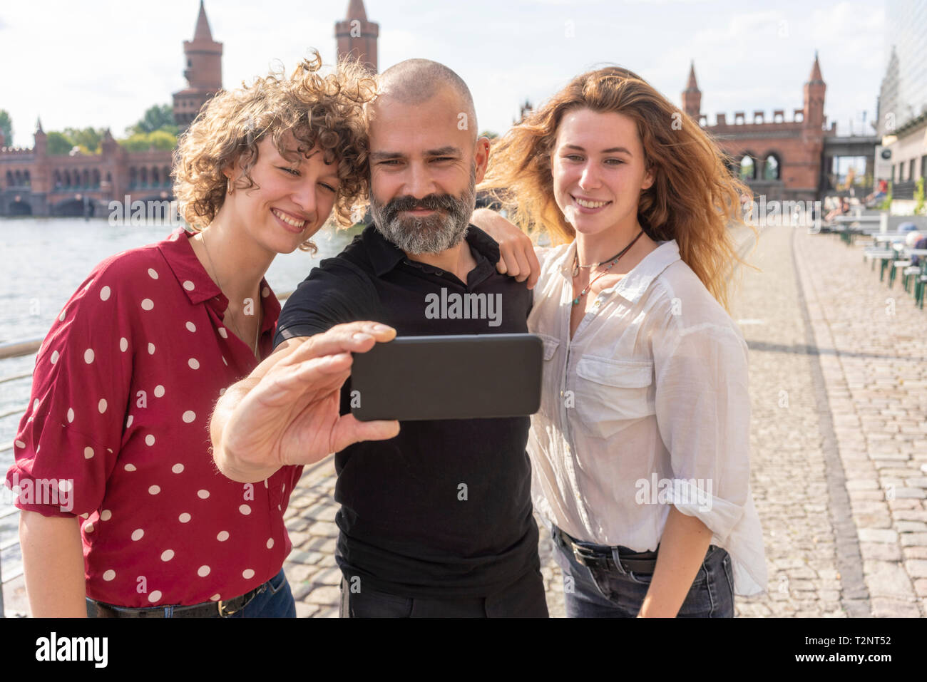 Mann und Frau Freunde unter selfie mit Smartphone auf der Brücke, den Fluss und die Gebäude im Hintergrund, Berlin, Deutschland Stockfoto