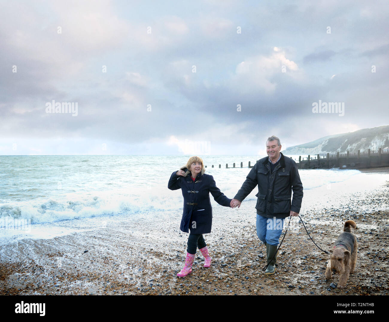 Romantische senior Paar halten sich an den Händen und gehen Hund am Strand, Eastbourne, East Sussex, England Stockfoto