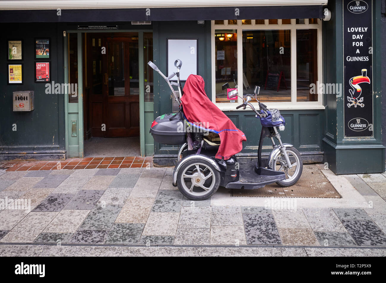 Tricyle Mobilität scooter mit Cover auf der Außenseite einen Irish Pub an einem regnerischen Tag in der Strand Street, Douglas, Isle of Man Stockfoto