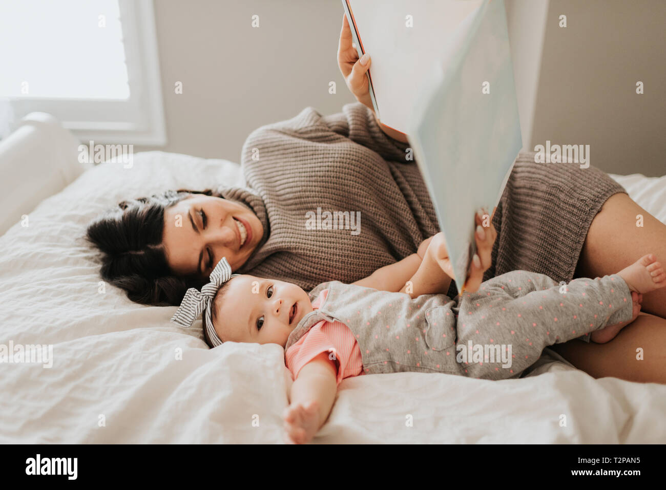Mutter Lesung mit Baby Tochter auf dem Bett im Schlafzimmer Stockfoto