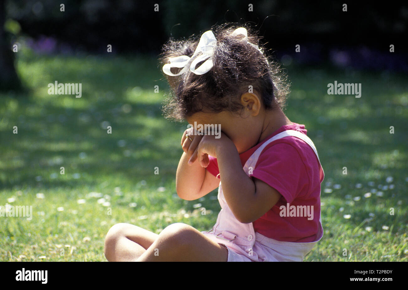 Kleines Mädchen im Garten sitzen die Augen reiben Stockfoto