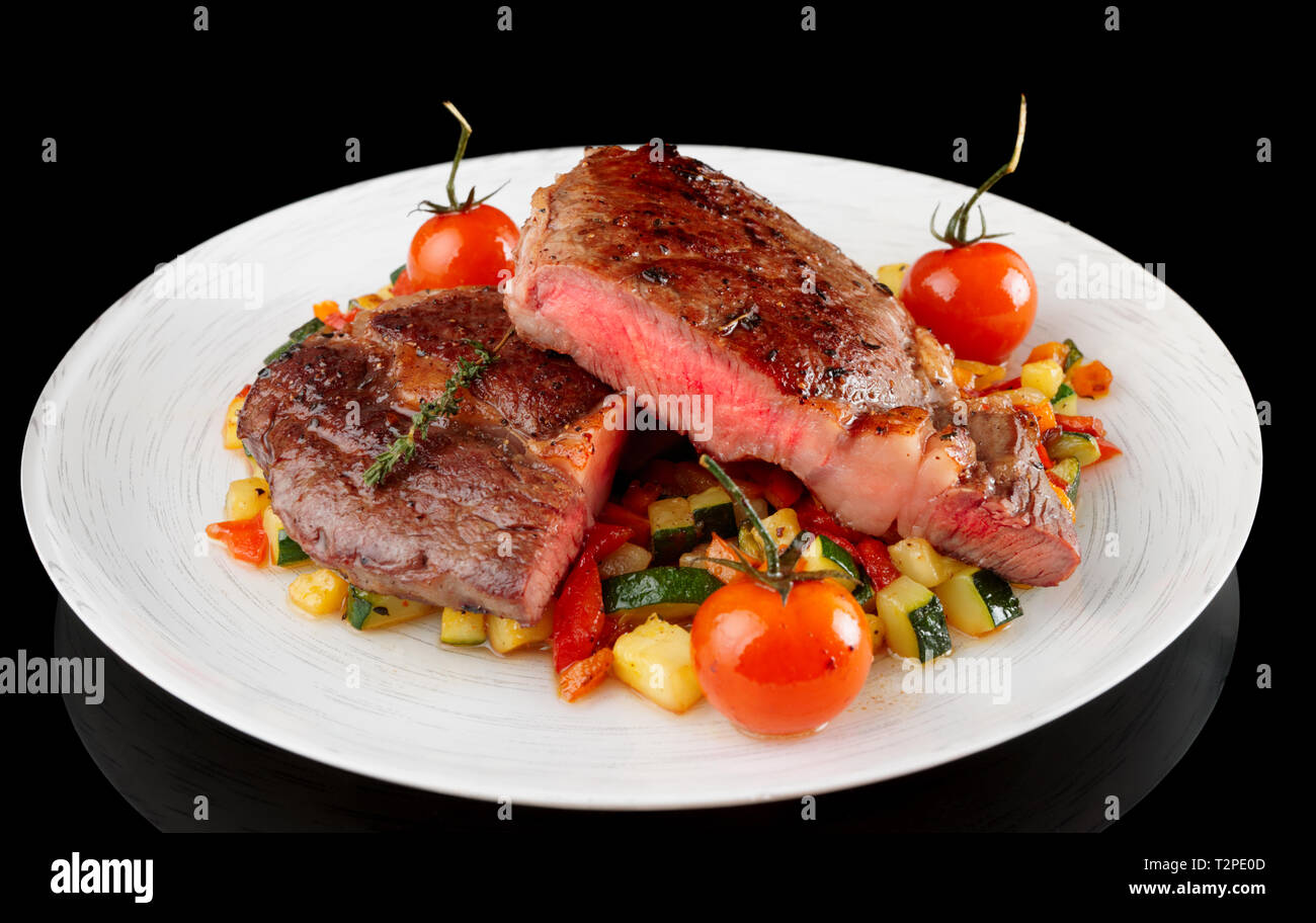 Medium gebratenes Steak mit gebratenem Gemüse Schuß auf schwarzem Hintergrund Stockfoto