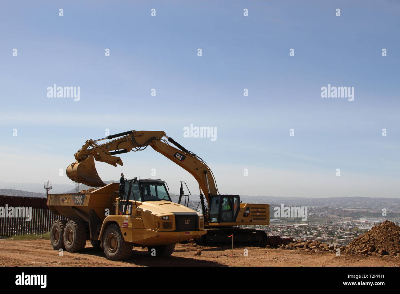 Suchen südwestlich von "Blechdose Hill", ein Bagger lasten Ablagerungen in einem Dump Truck vor bestehenden San Diego primäre Grenzmauer (links) für die San Diego sekundäre Grenzmauer am 29. März 2019. Das Corps ist die Unterstützung des Ministeriums für Innere Sicherheit fordern sie zusätzliche Grenzmauer in der Nähe von San Diego zu errichten. Stockfoto