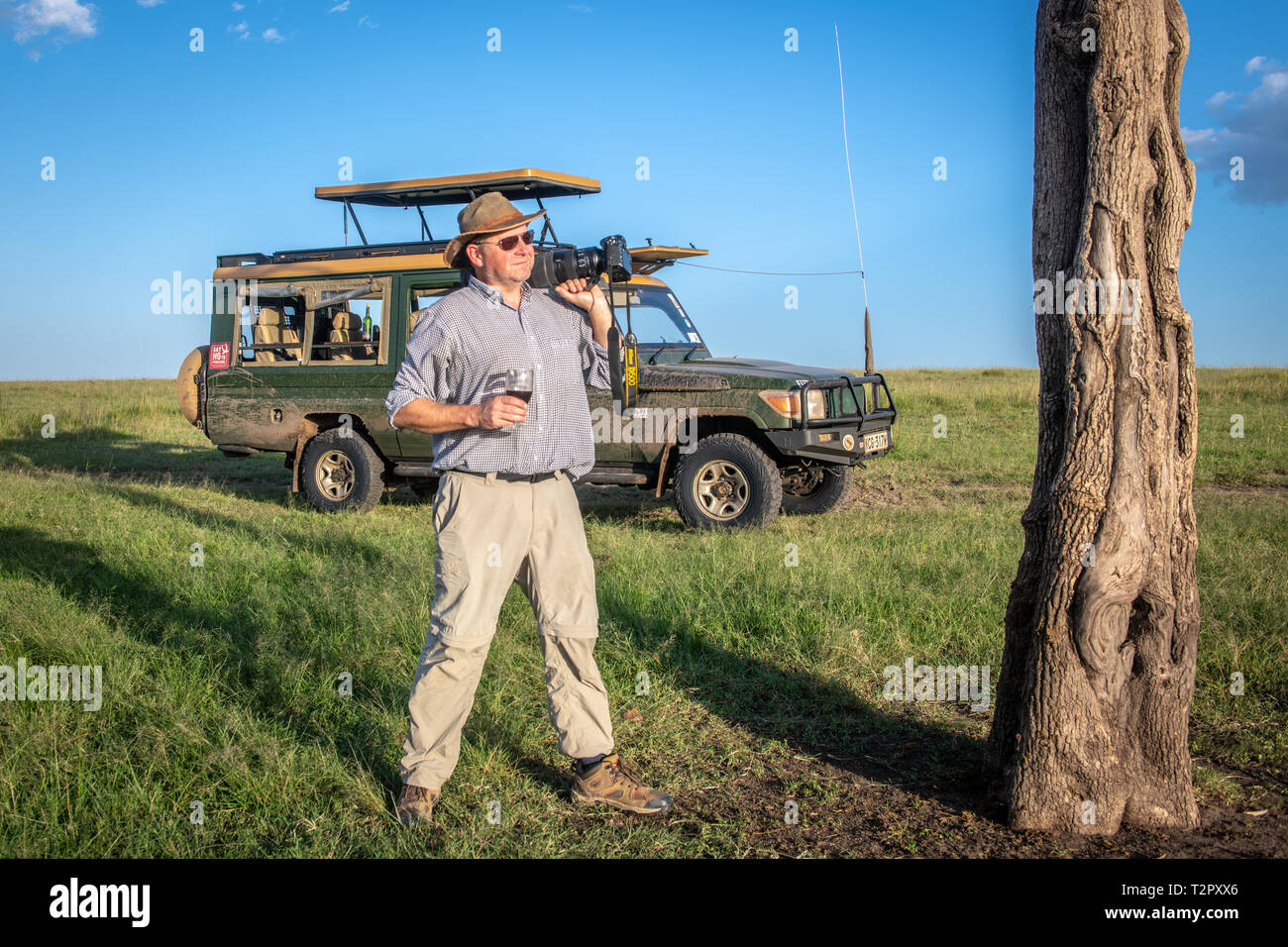 Der Fotograf hält seine Kamera und ein Drink vor einem Spiel Viewer in Masai Mara National Reserve, Kenia Stockfoto