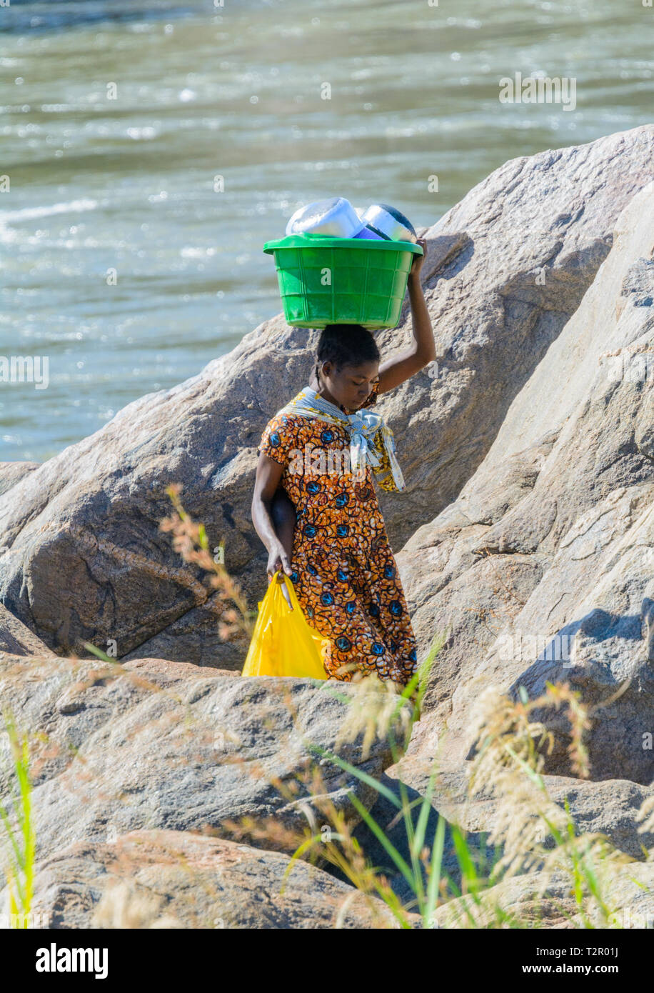 Malawische Frau Spaziergänge zwischen Felsbrocken auf Bank von Shire River, auf dem Kopf eine Schüssel von kochtöpfen sie im Fluss gewaschen hat Stockfoto