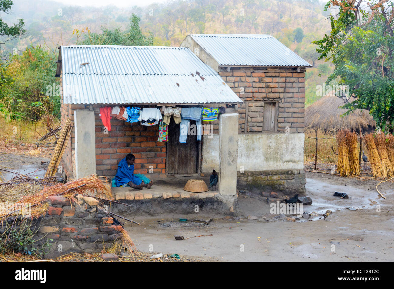 Malawische Dorf Frau Unterstände aus Unseasonal regen unter Eisen bedeckten Haus.jpg Stockfoto