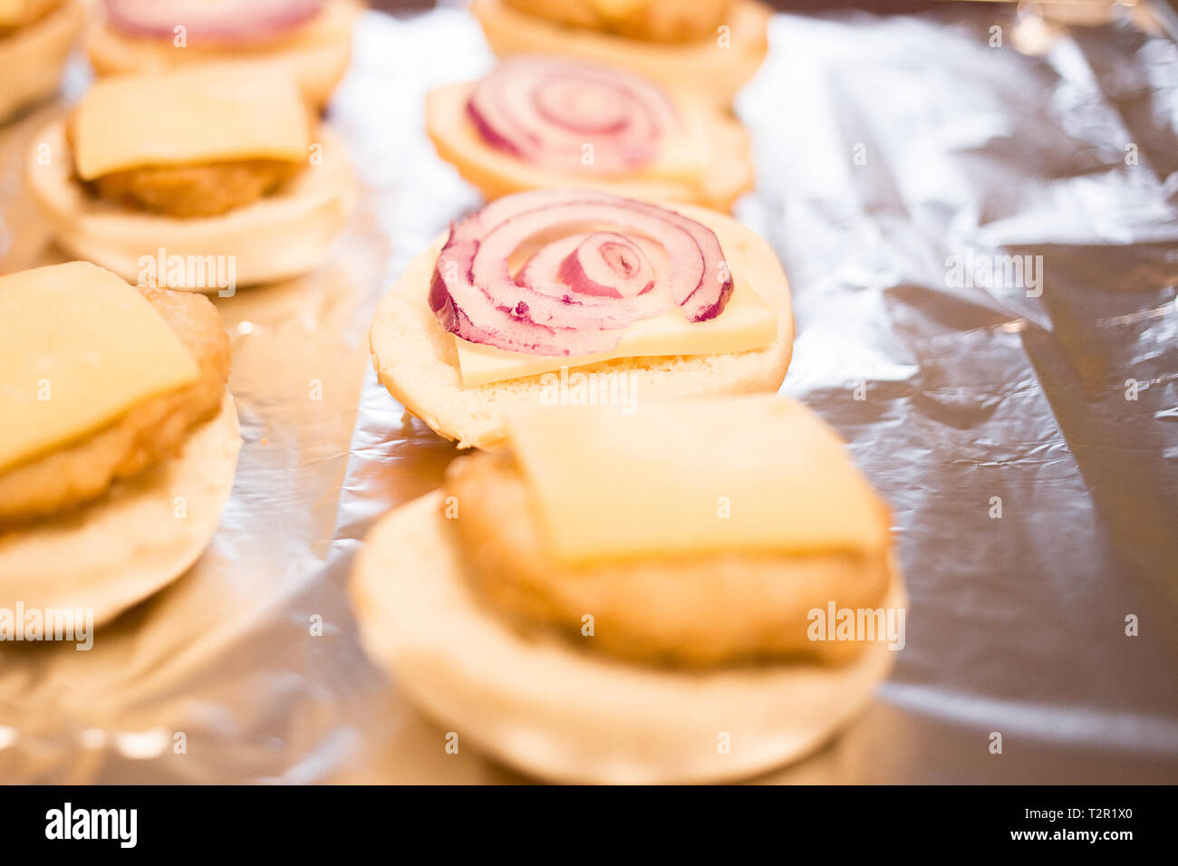 Mini Chicken Burger mit Käse werden auf eine silberne Folie gelegt, bevor sie in den Ofen gelegt wird; Stockfoto