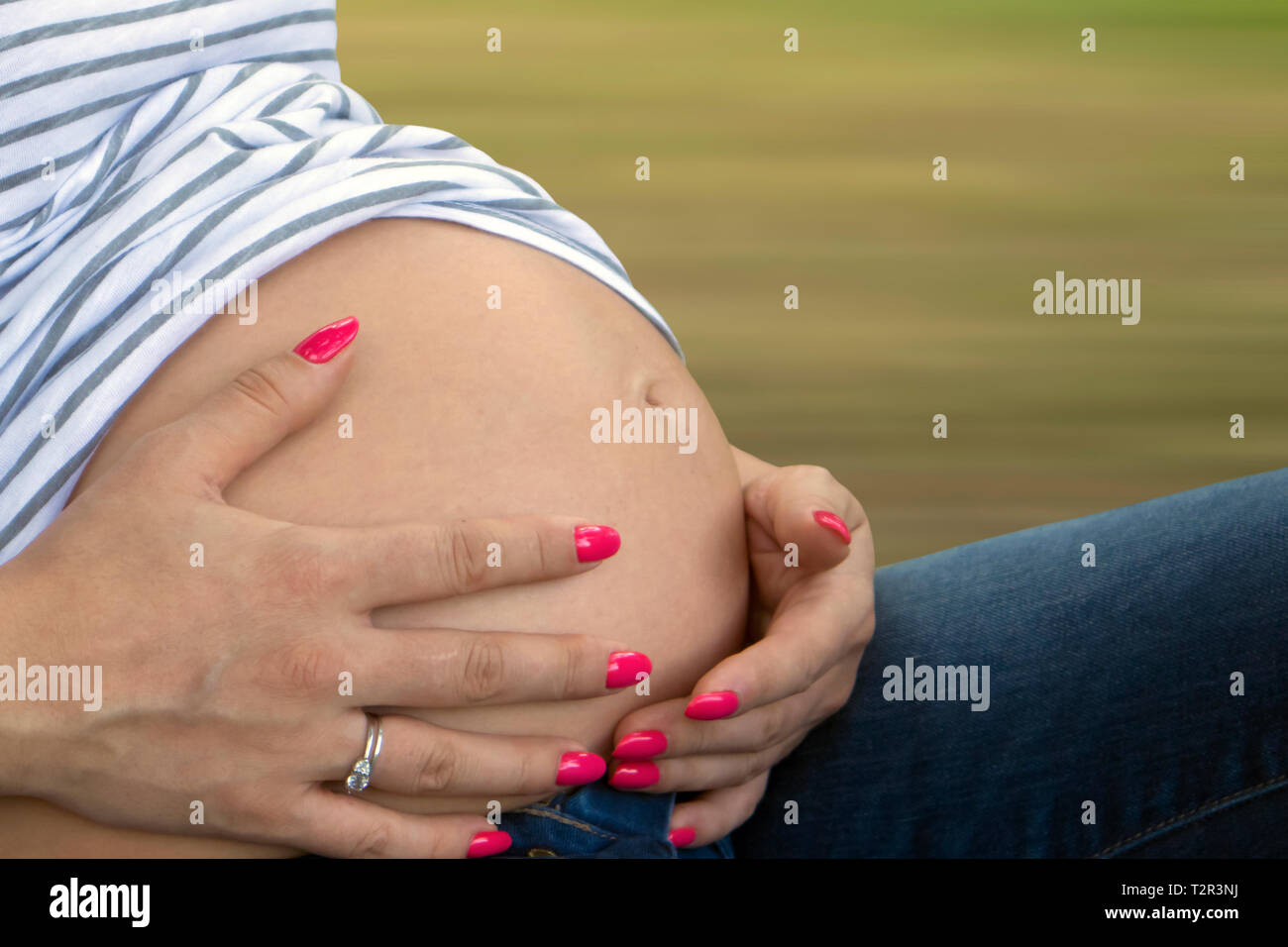 Schwangere niedlich Bauch und Frau Hände mit gepflegten Nägeln auf unscharfen pflanzliche Hintergrund isoliert Stockfoto
