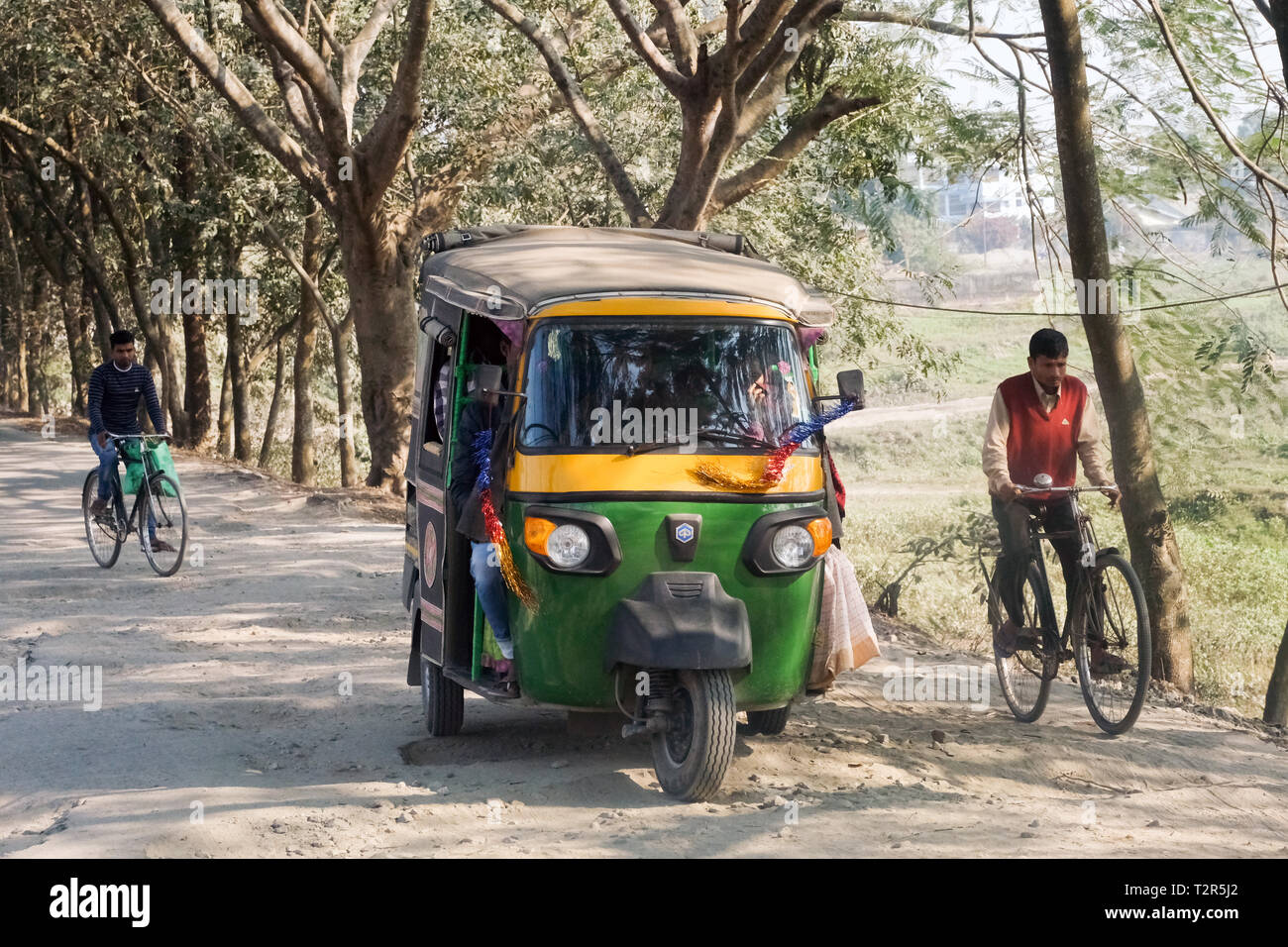 Motorrad Dreirad und Radfahrer auf einer schlechten Straße in Tangla, Assam, Indien --- Motorrad Dreirad und Radfahrer auf schlechter Straße im Ort Tangla, Bundesstaat Assam, Indien Stockfoto