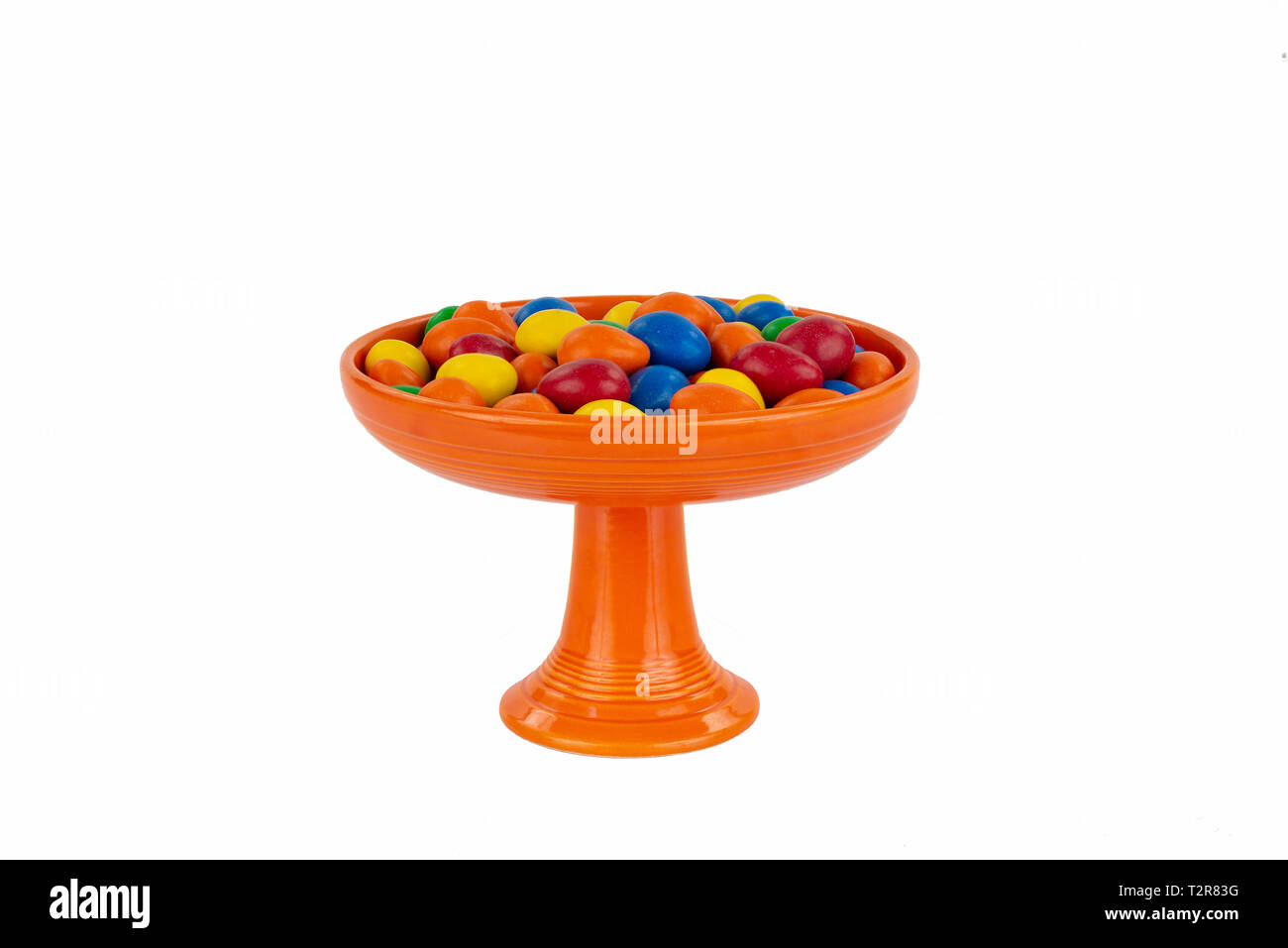 Helles Orange Vintage Fiesta Ware Sockel Candy Servierteller mit einer Auswahl an bunten Süßigkeiten. Anspruchsvolle und isoliert auf Weiss. Stockfoto