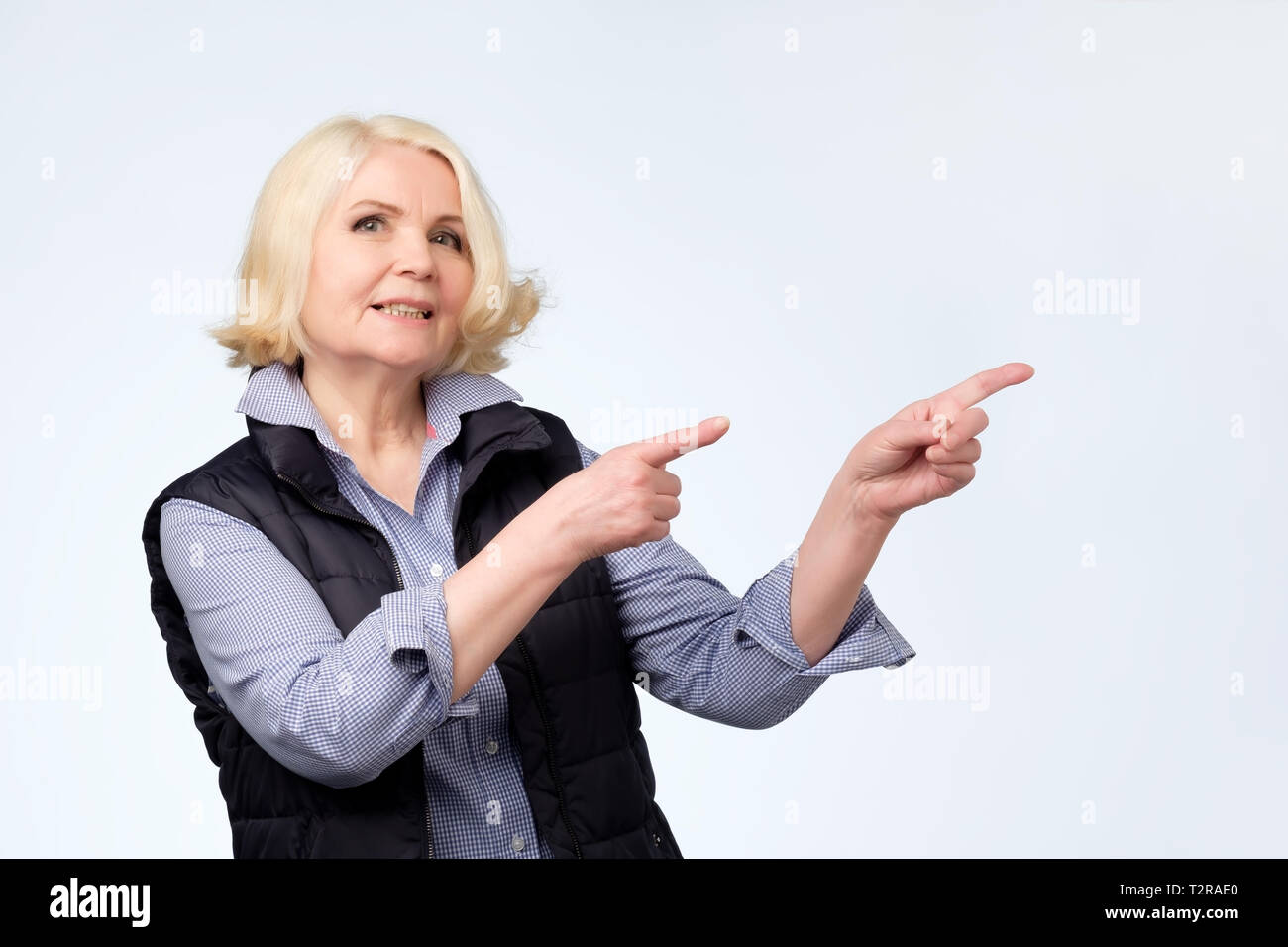 Gerne blonde ältere Frau lächelnd Pointing Finger weg, die etwas Interessantes und Spannendes in Studio Wand Stockfoto