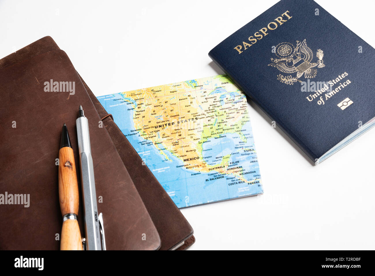 Eine Hochschule der amerikanischen Blaue Abdeckung Reisepass mit einem gefalteten Weltkarte, leder Zeitschriften, und Stifte auf einem schlichten weißen Hintergrund. Stockfoto