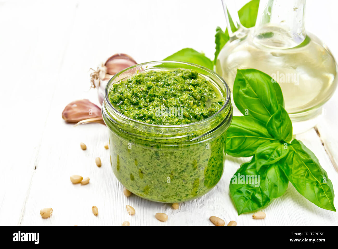 Pesto in einem Glas, Basilikum, Pinienkerne, Knoblauch und Olivenöl in eine Karaffe auf einem Holzbrett Hintergrund Stockfoto