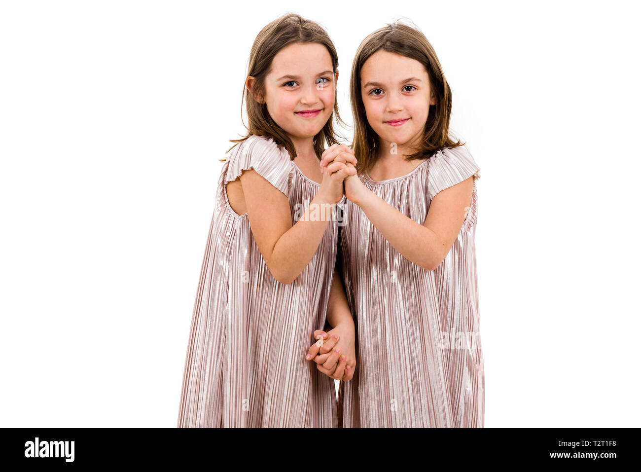 Identische Zwillinge Schwestern sind posieren für die Kamera. Happy Zwillingsschwestern in den Kleidern suchen nach Kamera, lachen, lächeln, halten sich an den Händen. Frontairbags Stockfoto