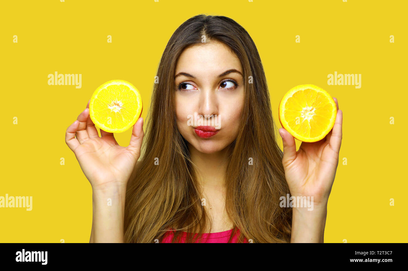 Closeup Portrait verwirrt, ratlos, unglücklich, nachdenkliche junge Frau, Mädchen, halten zwei halbe Orange, unsicher, es zu essen. Menschliches Gesicht Ausdrücke, emoti Stockfoto