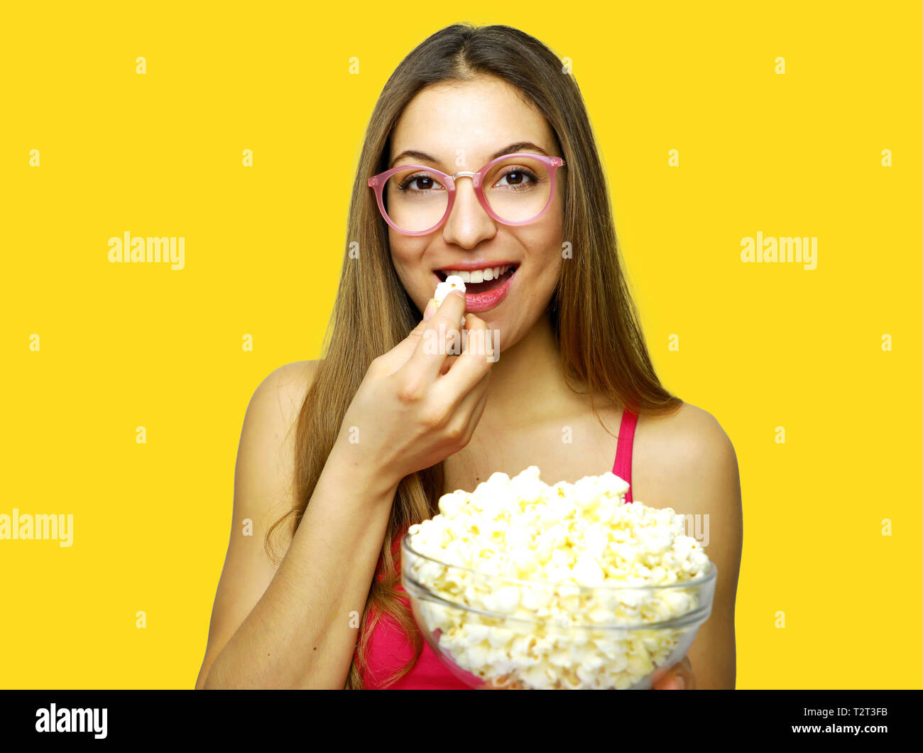 Gerne fröhliche Frau essen Pop Corn auf gelben Hintergrund. Mädchen, dass große Glasschüssel mit Kino Teil des Pop Corn. Stockfoto