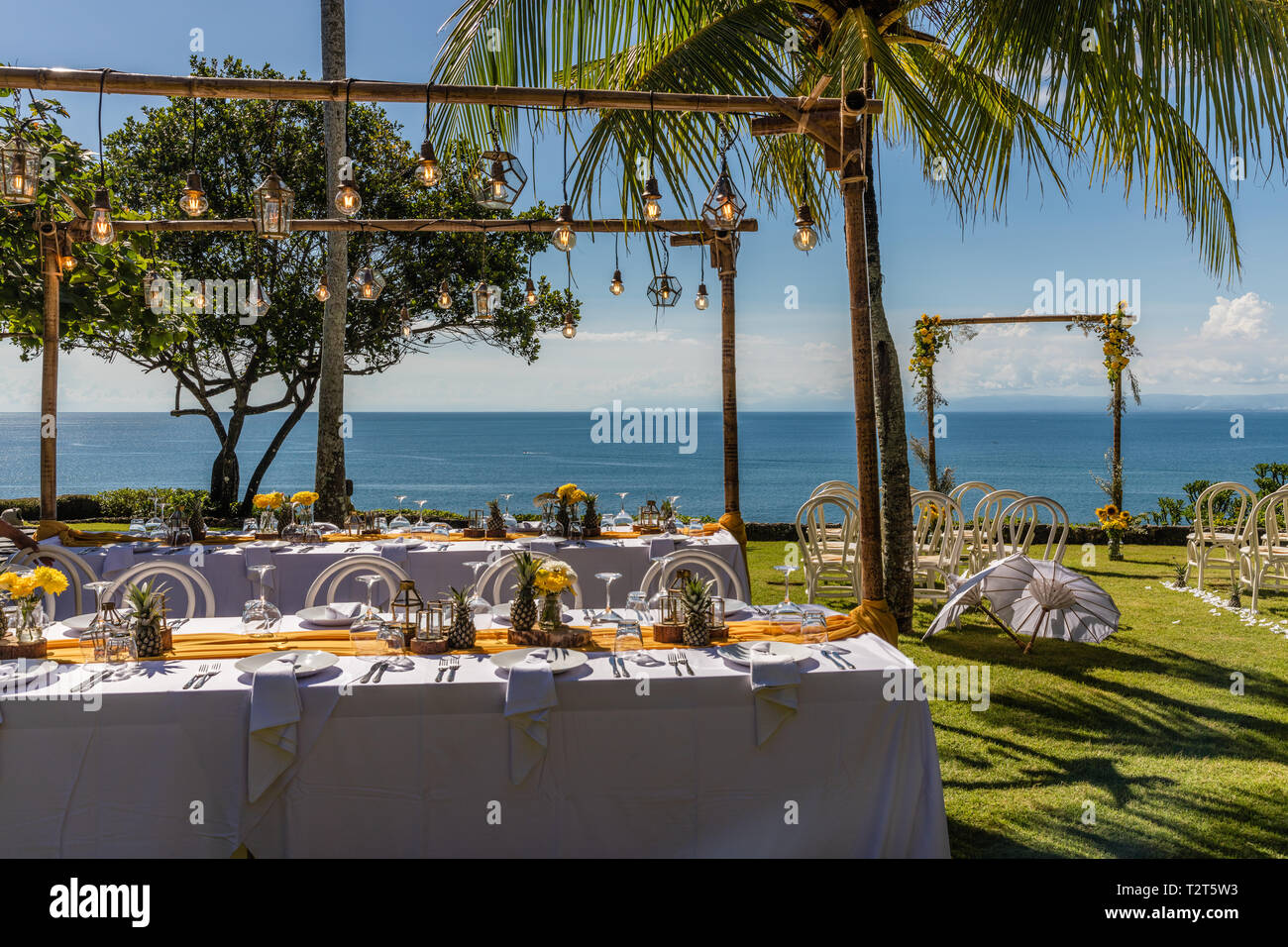 Weiß gedeckten Tischen für Hochzeit Abendessen mit gelben Rosen, Chrysanthemen, Ananas und Glas Lampen eingerichtet. Blick auf das Meer. Hochzeit. Stockfoto