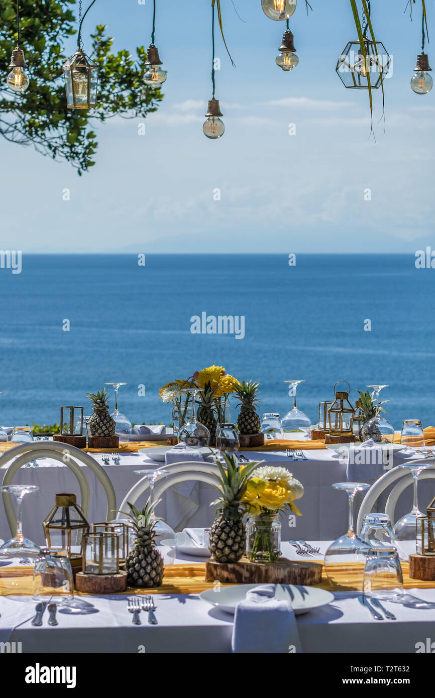 Weiß gedeckten Tischen für Hochzeit Abendessen mit gelben Rosen, Chrysanthemen, Ananas und Glas Lampen eingerichtet. Blick auf das Meer. Hochzeit. Stockfoto