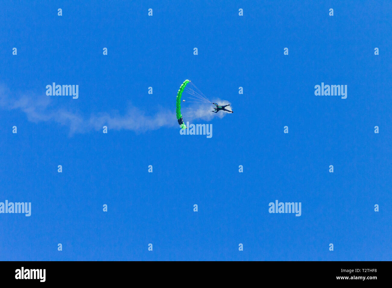 Fallschirmspringer Fallschirmspringen fliegen mit open green Fallschirm Wendungen und biegen Sie in Richtung Erde im blauen Himmel. Stockfoto