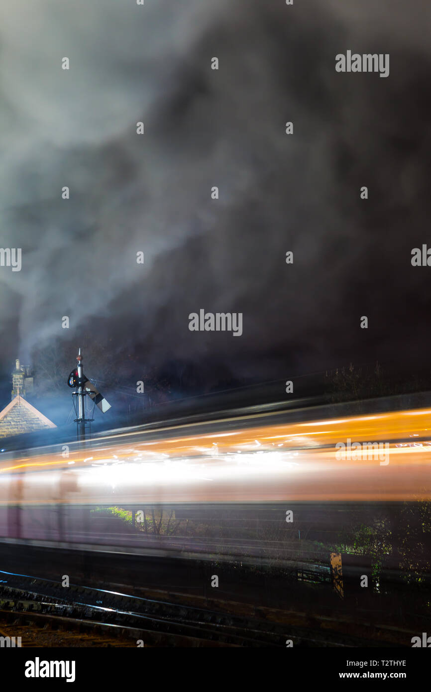 Atmosphärisch, Moody Nacht und beweglichen UK Dampflok durch Vintage Railway Station in der Nacht unterwegs. Lange Belichtung: Bewegung, Bewegungsunschärfe. Stockfoto