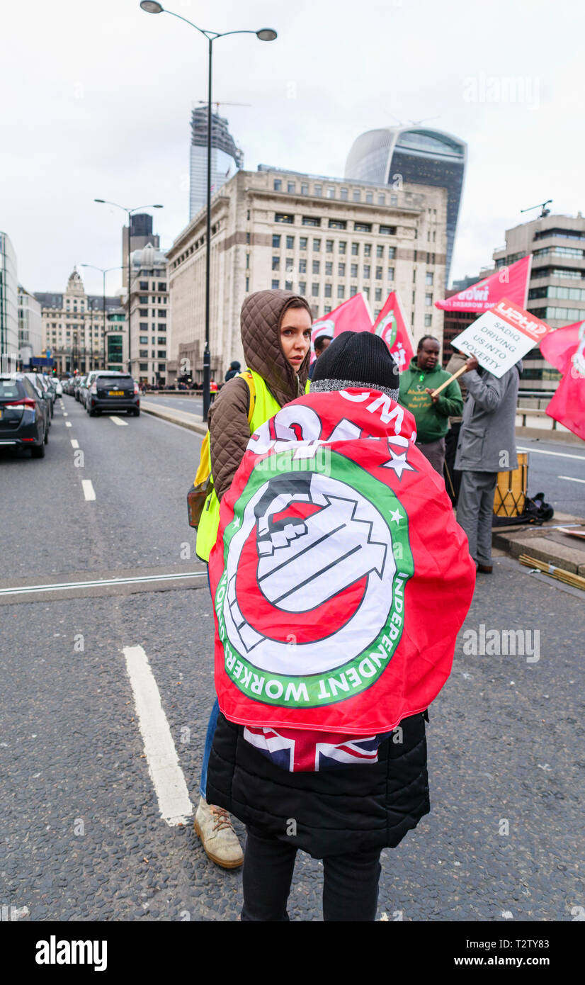 London, UK, 04. April 2019. Minicab Treiber Block die Straße auf die London Bridge protestieren gegen die Verkehrsüberlastung auf private Hire minicabs. Dieser Demonstrator ist in die rote Fahne der IWGB (Unabhängige Gewerkschaft in Großbritannien) gewickelt. Credit: Graham Prentice/Alamy leben Nachrichten Stockfoto