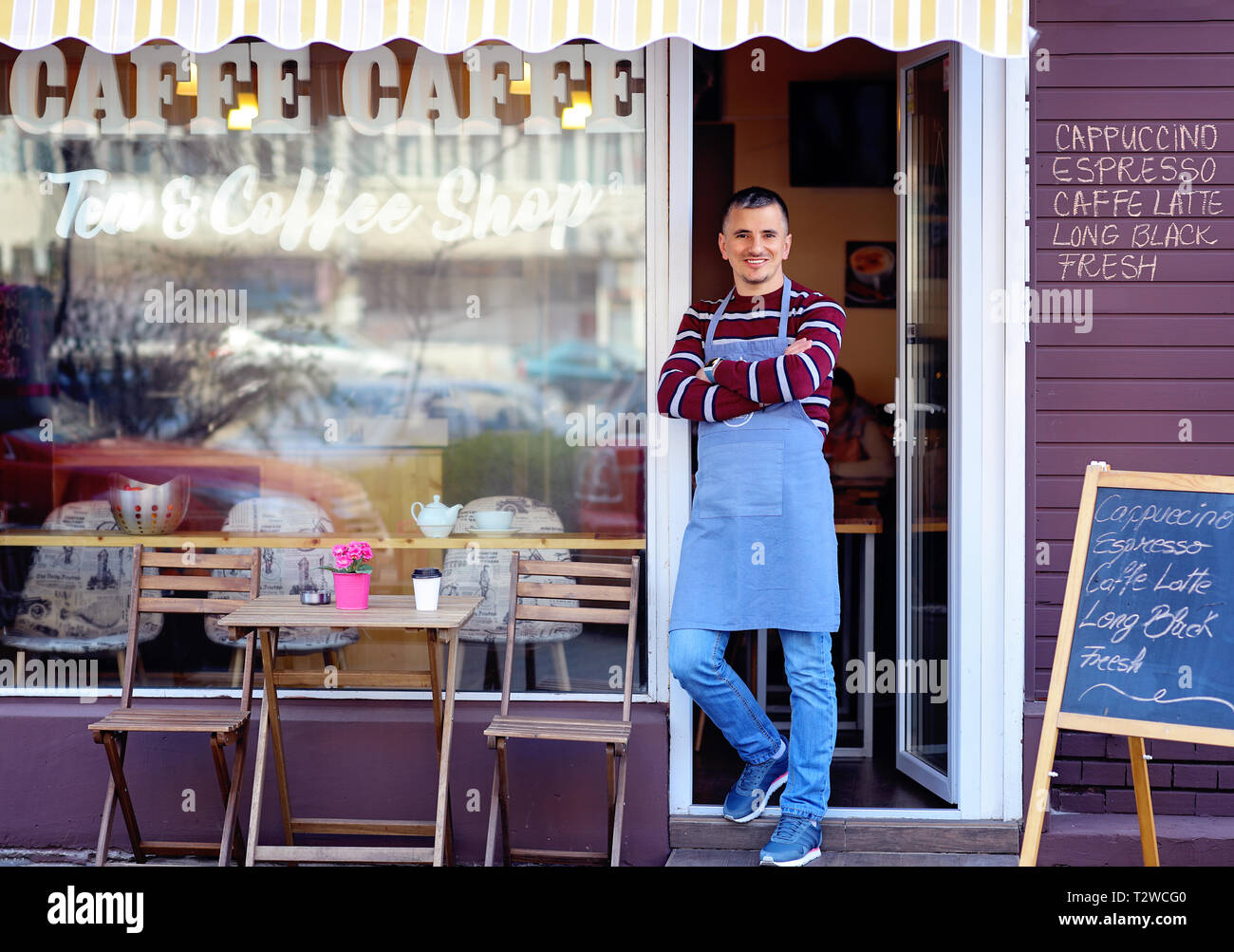 Porträt einer selbstbewussten jungen Mann in der Tür einen Coffee Shop. Tee und Kaffee Shop auf dem Fenster geschrieben. Verkehr Reflexion. Seine welcomi Stockfoto
