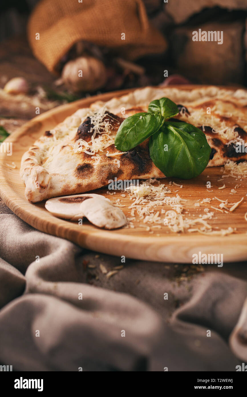 Auf einem Holzbrett, Pizza Calzone, Basilikum, Pilzen und geriebenem Käse. Poster für Restaurants oder Pizzerien Stockfoto