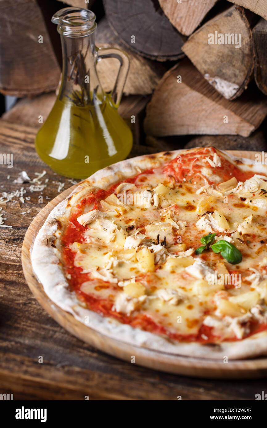 Pizza mit Huhn und Ananas auf dem Hintergrund von Brennholz. Konzept Werbe-flyer. Pizza auf einer hölzernen Hintergrund Stockfoto
