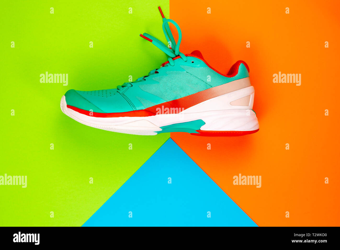 Rot, Hellblau, Weiß neu Tennisschuh im Studio Schuß über grün, orange, blau Hintergrund. Direkt von oben. Stockfoto