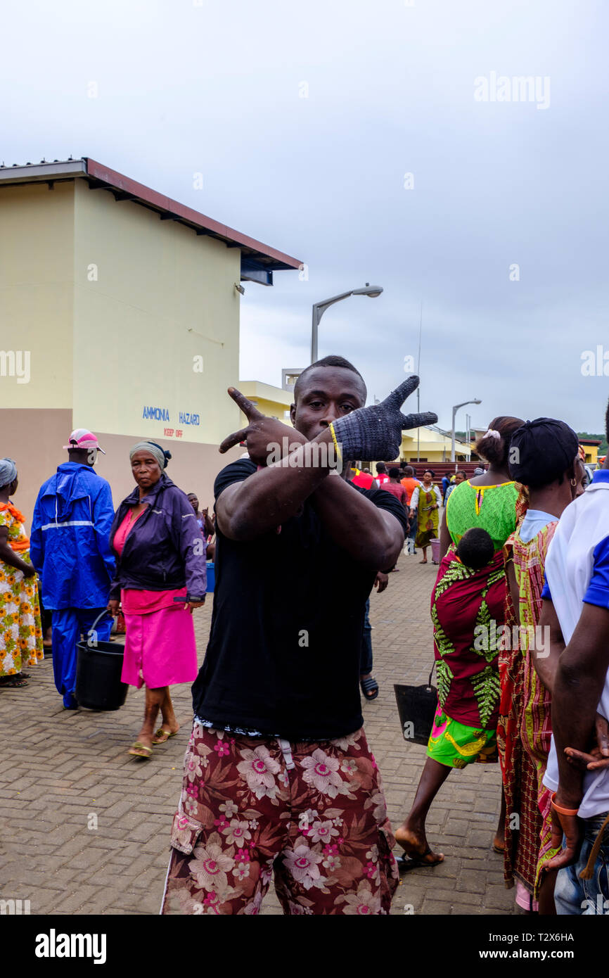 SEKONDI TAKORADI, GHANA - 10. APRIL 2018: Junge männliche Arbeiter tragen einen Handschuh an belebten Bosomtwi Sam Fischer Hafen Fischmarkt kreuzt seine Arme und Mak Stockfoto