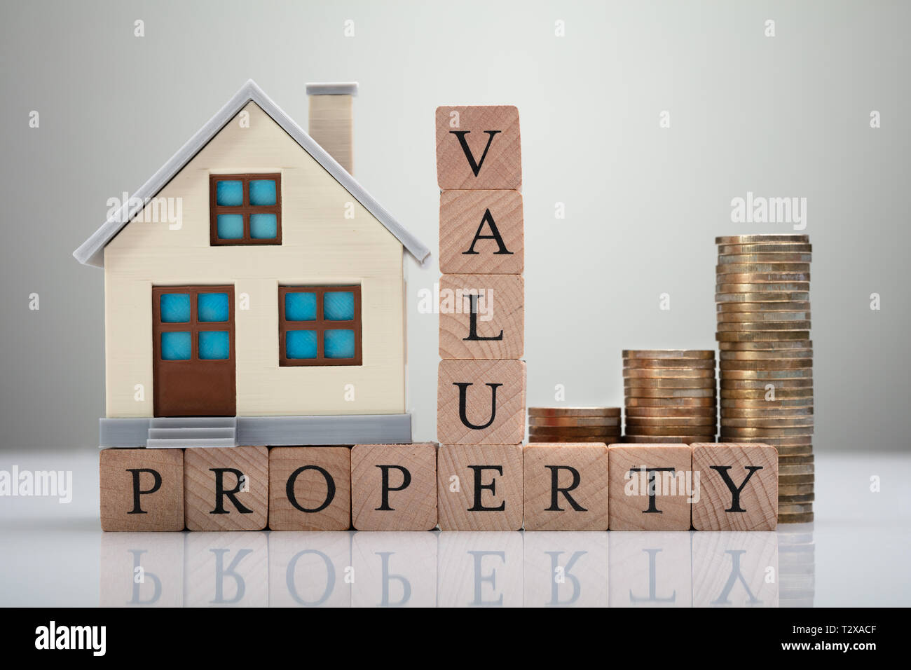 Haus Modell und gestapelte Münzen zeigen Property Value Konzept auf reflektierenden Schreibtisch Stockfoto