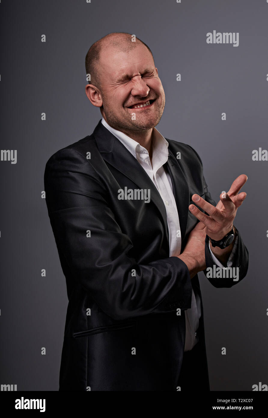 Verlassen kahlen business Mann im schwarzen Anzug, der die Hände erfolg Sieger Zeichen auf grauem Hintergrund. Closeup Portrait Stockfoto