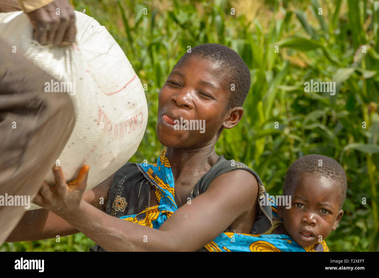 Frau mit Baby auf dem Rücken sammeln Tasche von Mais als Relief Stockfoto