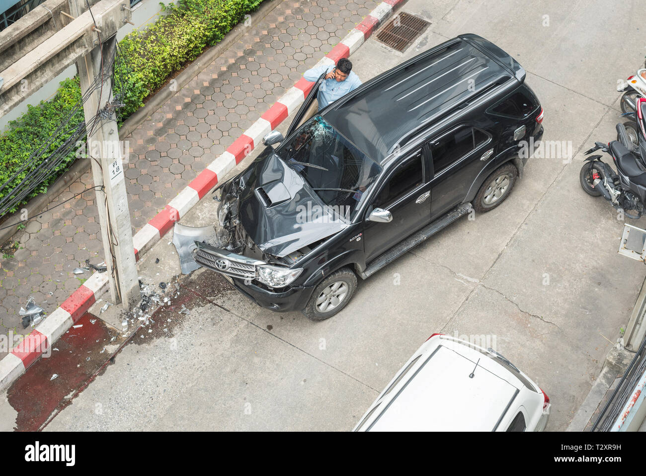 Bangkok, Thailand - 12. Dezember 2018: ein Auto Besitzer macht einen Anruf nach Absturz mit seinem Wagen gegen einen Strommast in einem leeren Backstreet. Stockfoto