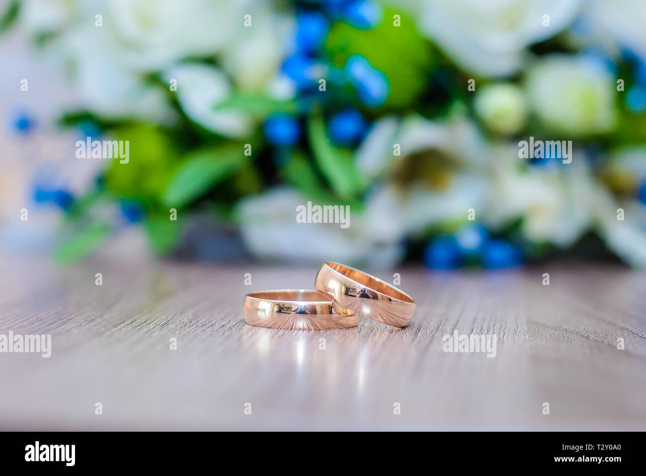 Schönen gold Trauringe auf den Tisch neben Blumenstrauß für die Braut in Weiß und Blau Blumen Stockfoto