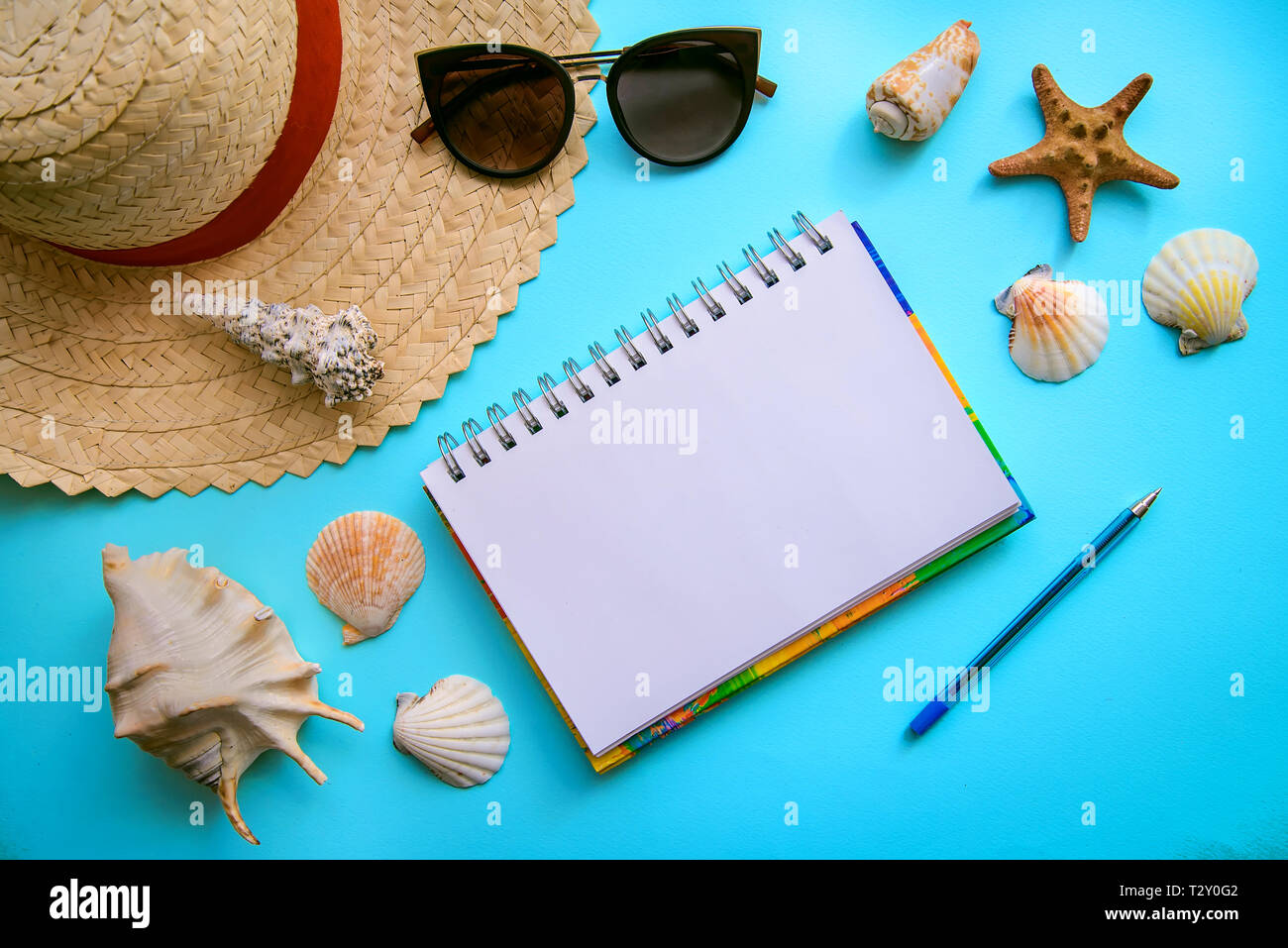 Das Layout auf das Thema Urlaub am Meer: Stroh Hut, Sonnenbrille, Muscheln und Notizblock mit Stift auf einem blauen Hintergrund, Ansicht von oben Stockfoto